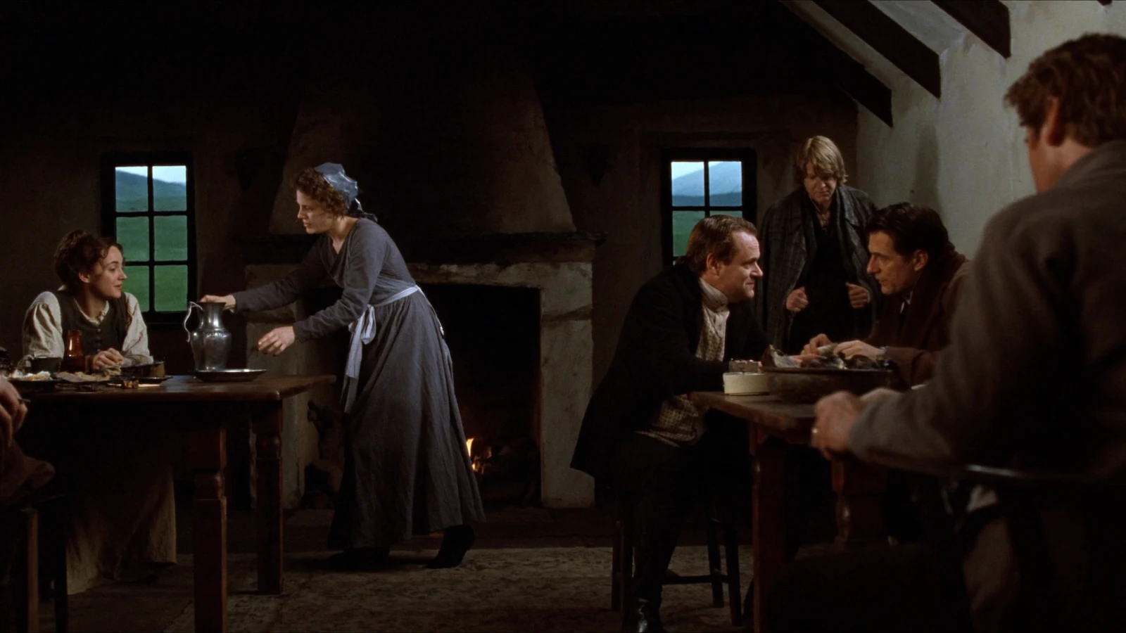 Villagers eat and talk while a woman serves supper in the Scottish inn